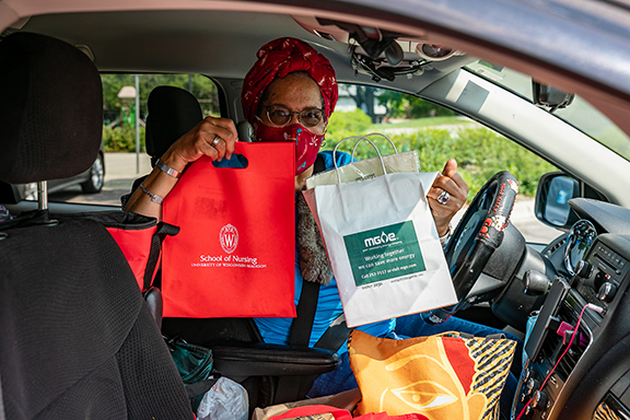 woman wearing a mask in a car holding up bags from a drive-through resource fair