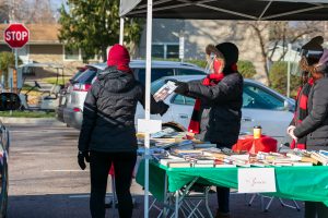 a person in a winter parka hands a book to another person during an outdoor event