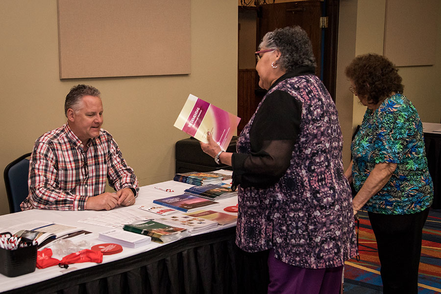 woman picking up educational resources from man sitting at table full of brochures