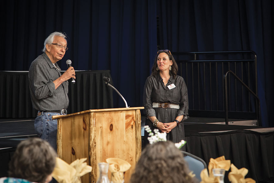 man speaking to a crown at a podium with woman looking on